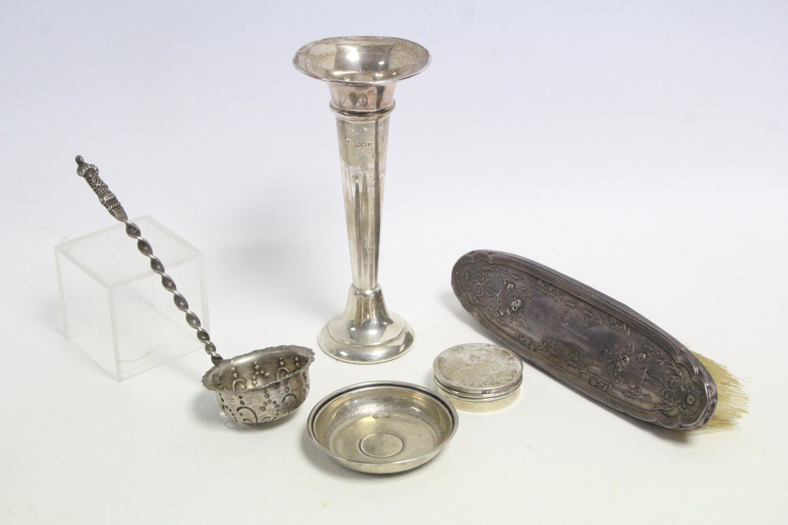 A silver backed clothes brush; a silver sifter spoon; a silver spill vase; & two other silver