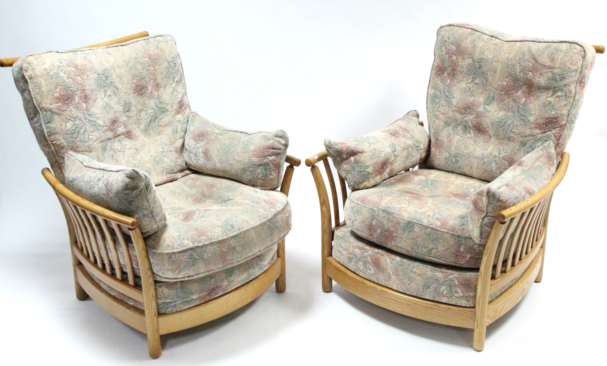 A pair of Ercol light elm frame armchairs with loose cushions to the seats & backs, & on short round