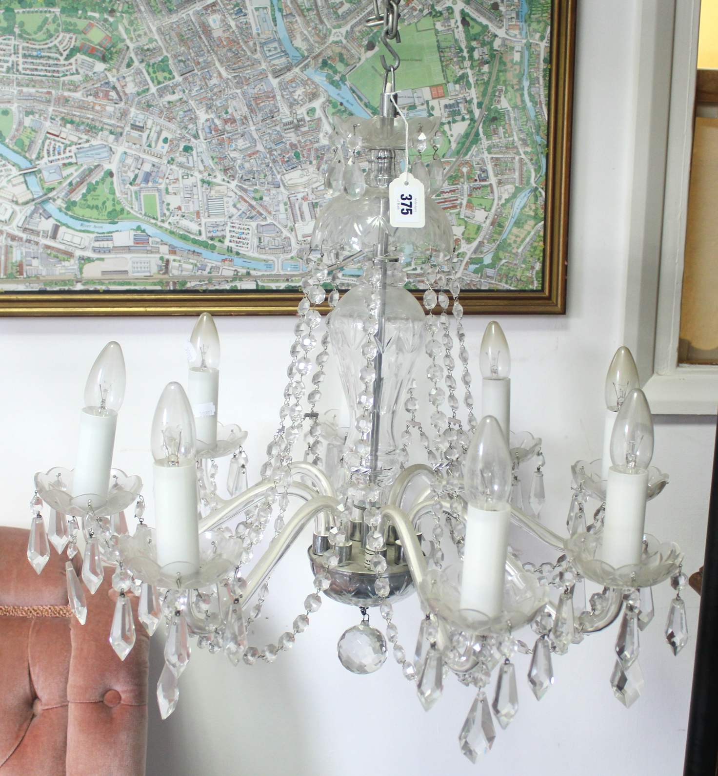 A cut glass chandelier with eight scroll arms with pendant prism drops, the slender baluster