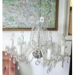 A cut glass chandelier with eight scroll arms with pendant prism drops, the slender baluster