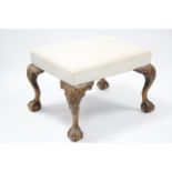 A George II-style carved walnut stool, the rectangular padded seat upholstered cream fabric, on