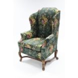 An early 18th century-style upholstered wing-back armchair on square cabriole legs with shaped