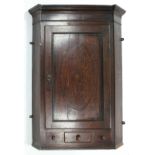 An early 19th century oak hanging corner cupboard fitted three shaped shelves enclosed by a