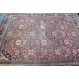 A Persian carpet with all-over multicoloured repeating stylised floral design on a coral-red ground,