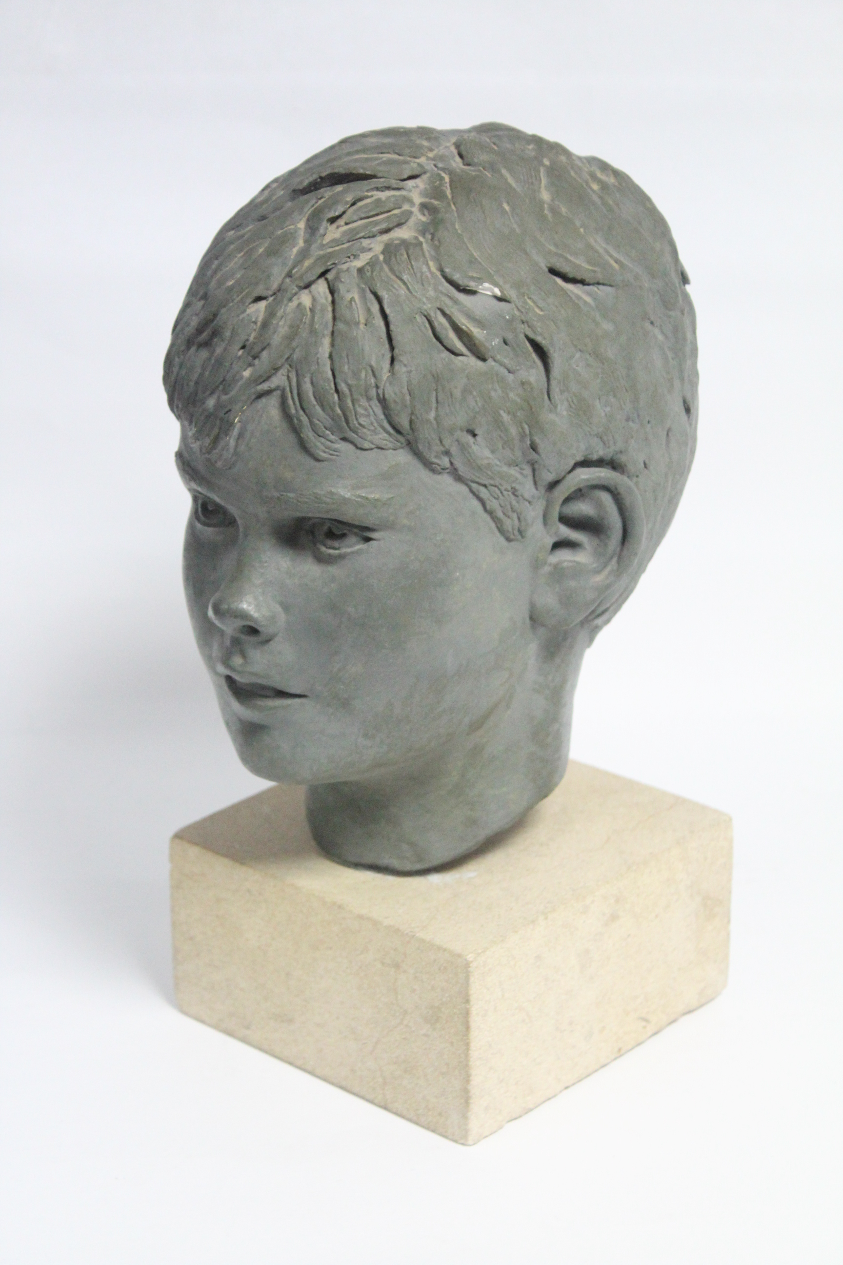 A green painted plaster head of a young boy, on stone block base; 13½” high over-all.