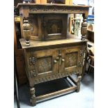 A reproduction small carved oak court cupboard the upper part enclosed by centre panel door, the