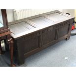AN ANTIQUE OAK COFFER, with hinged lift-lid, panelled sides, & on square supports (reduced in