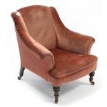 A late Victorian easy chair upholstered pink velour, & on short turned legs with ceramic castors.