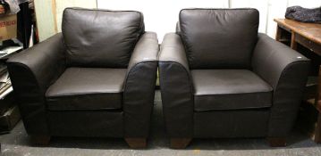 A pair of brown leather armchairs with square backs, loose cushions, & on block feet.