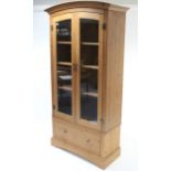 A pine tall standing cabinet with rounded top, fitted three shelves enclosed by pair of glazed doors