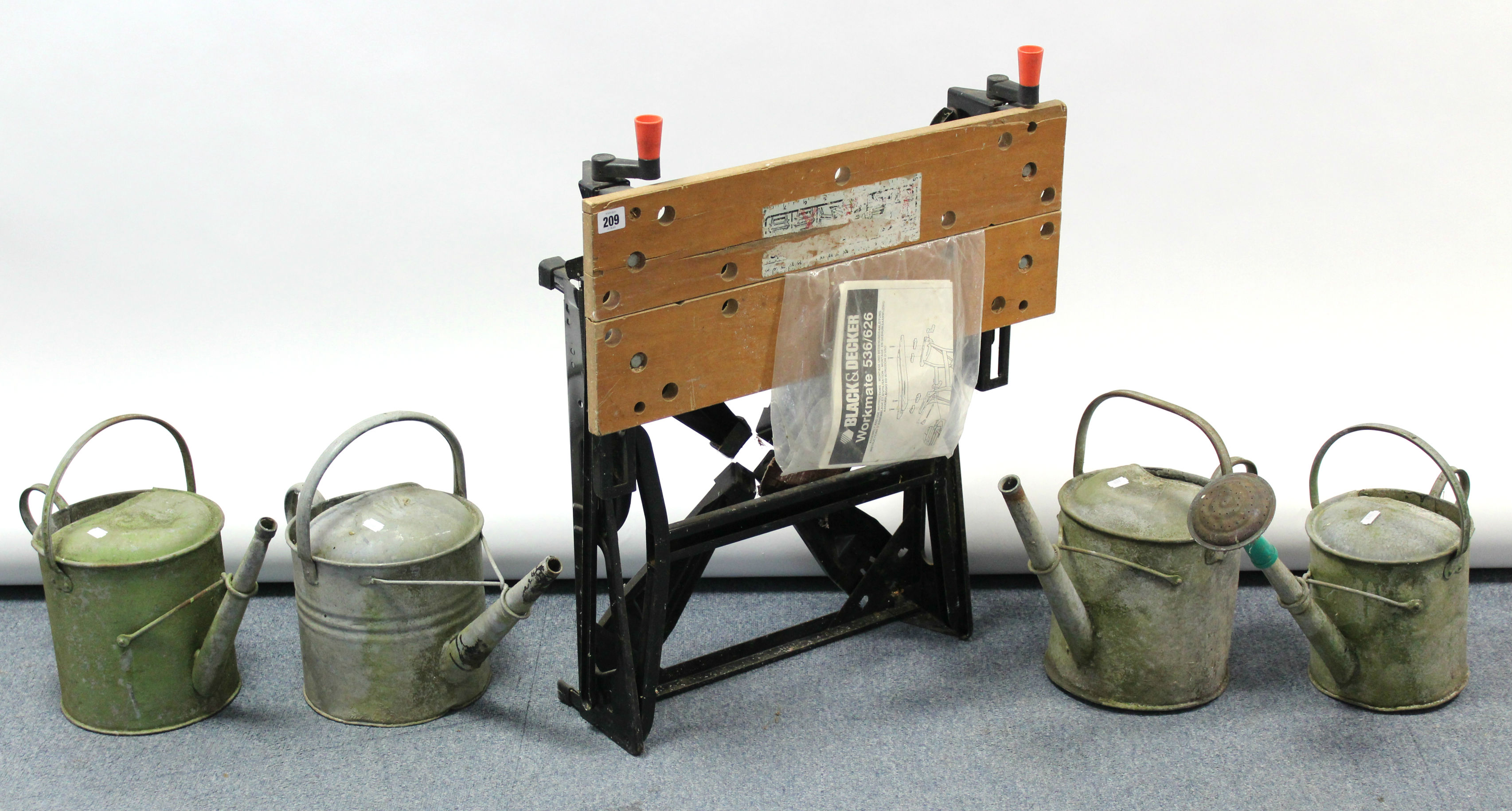 A black & Decker “workmate” & four galvanised metal watering cans.