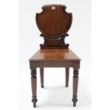 A regency mahogany hall chair with shaped panel back, hard seat, & on turned tapered legs.