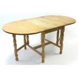 A light oak drop-leaf dining table on turned legs with plain stretchers, 64¾” x 34¾”.
