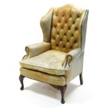 An 18th century-style wing-back armchair upholstered brass-studded mustard yellow leather, with