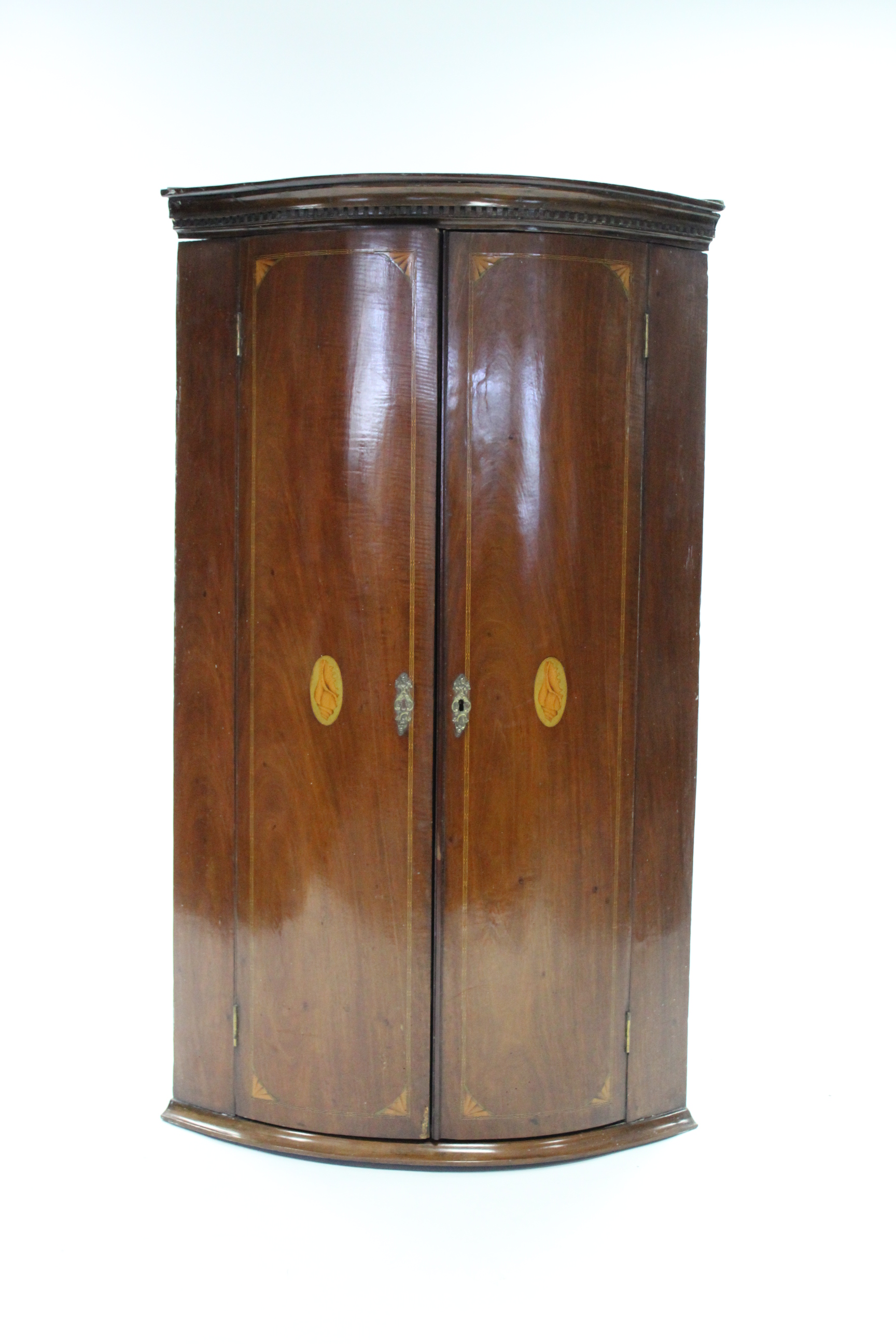 An early 19th century inlaid-mahogany bow-front corner cupboard, with dentil cornice above a pair of