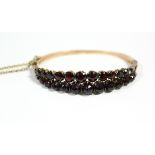 A continental gold stiff hinged bangle set two rows of graduated garnets.