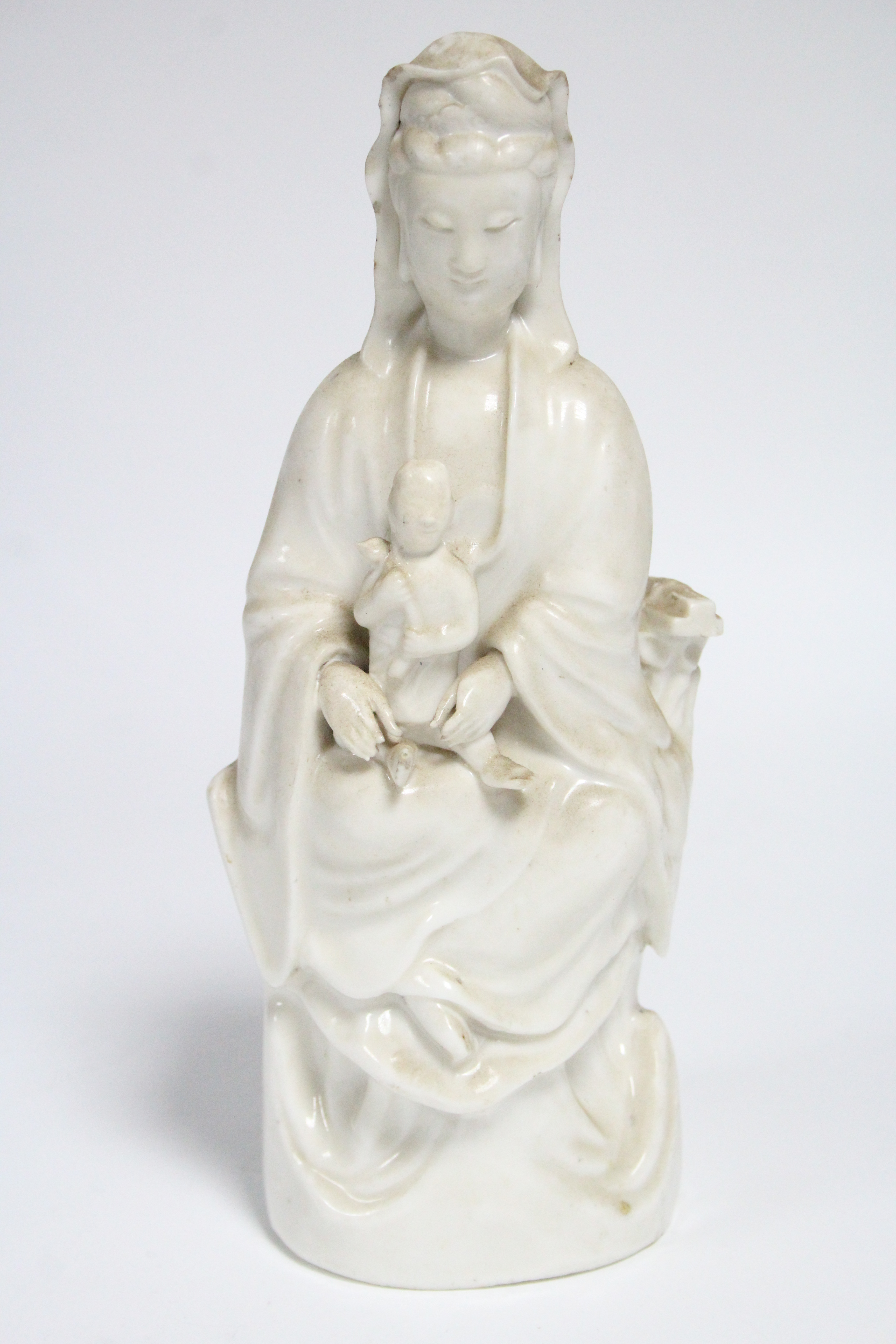 An 18th century Chinese blanc-de-chine figure of Guanyin, seated, with an infant on her lap; 10”