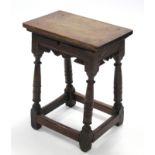 A 17th century oak joint stool, with shaped apron & on ring-turned tapering legs with stump feet