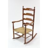 A beech ladder-back rocking chair with woven-rush seat.