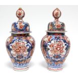 A pair of 19th century Japanese Imari fluted baluster vases with domed covers; 12” high.