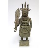 A Benin bronze standing figure of a warrior, in traditional dress & holding a sword in one hand,
