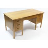 A mid-20th century light oak finish kneehole desk, cited with an arrangement of two brushing