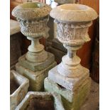 A pair of reconstituted stone garden urns of round tapered form, with grotesque masks to sides, & on