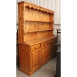 A pine dresser, the upper part fitted two open shelves & with panelled back, the base fitted four