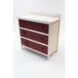 A white & crimson painted oak small chest fitted three long drawers with turned knob handles, & on