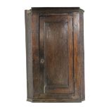 A late 18th century oak corner cupboard, fitted three shelves enclosed by a fielded panel door;