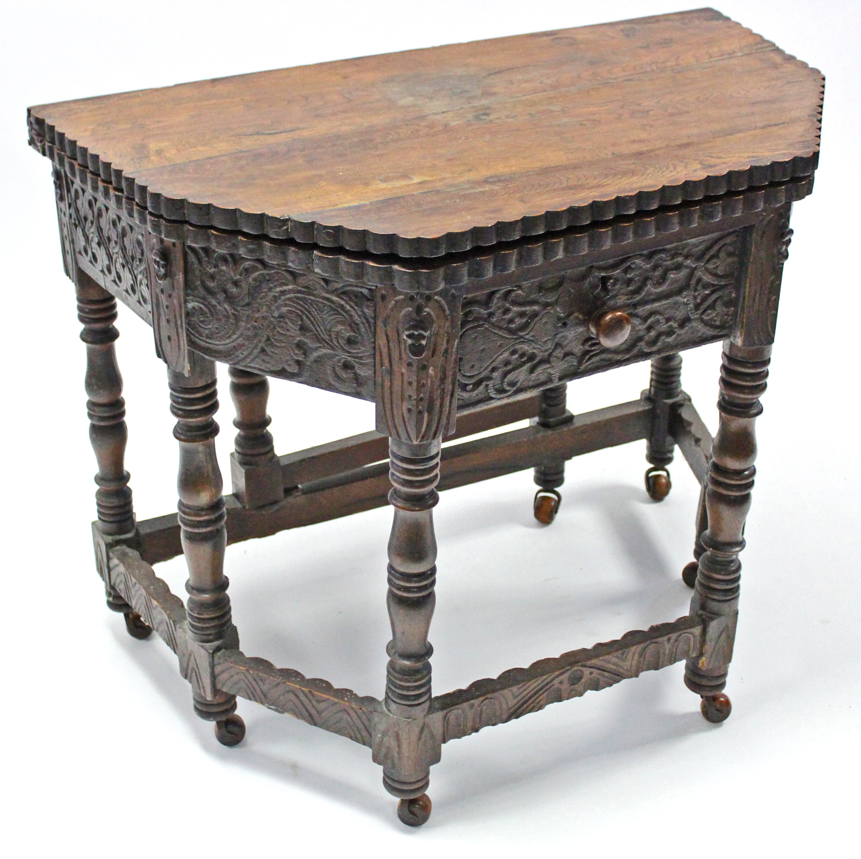 A 17th century-style carved oak credence table with fold-over top, shaped edge, fitted frieze