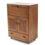 AN ERCOL LIGHT ELM SIDE CABINET with fall-front above cupboard enclosed by pair of panel doors,