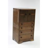 A mid-20th century small oak millinery cupboard, enclosed by pair of panel doors above four long