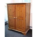 A pine millinery cupboard fitted two shelves enclosed by pair of fielded panel doors, & on shaped