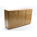 AN ERCOL LIGHT ELM SIDEBOARD fitted three frieze drawers above cupboard enclosed by three panel