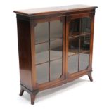 A mahogany bookcase with two adjustable shelves enclosed by pair of glazed doors, & on shaped plinth