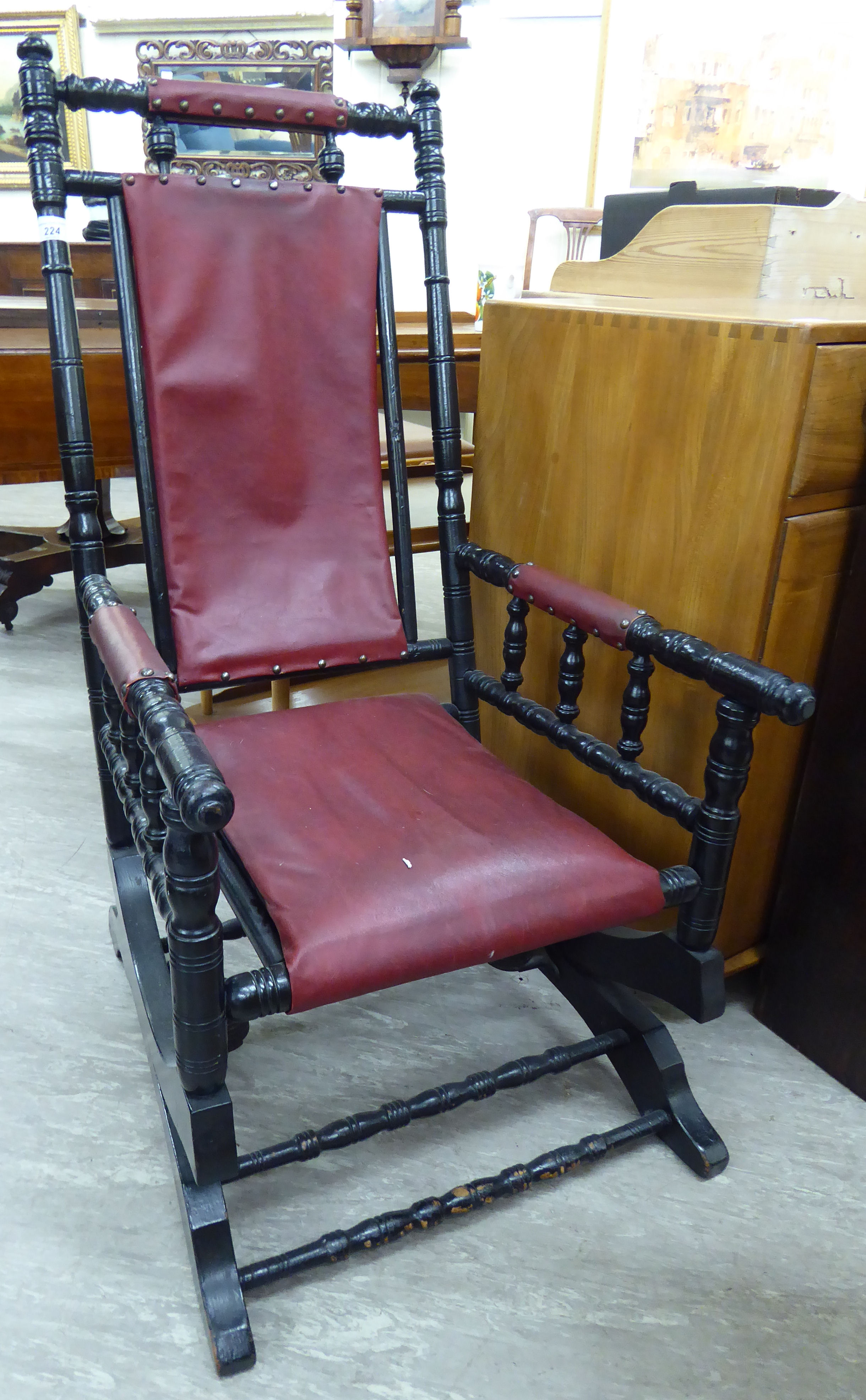 A late 19thC American ebonised hardwood framed rocking chair with a red faux hide upholstered back