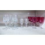A set of six cranberry coloured glass stemmed wines; six cut glass sherries;