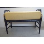 A modern black painted faux bamboo duet stool with a cushion covered, caned seat,