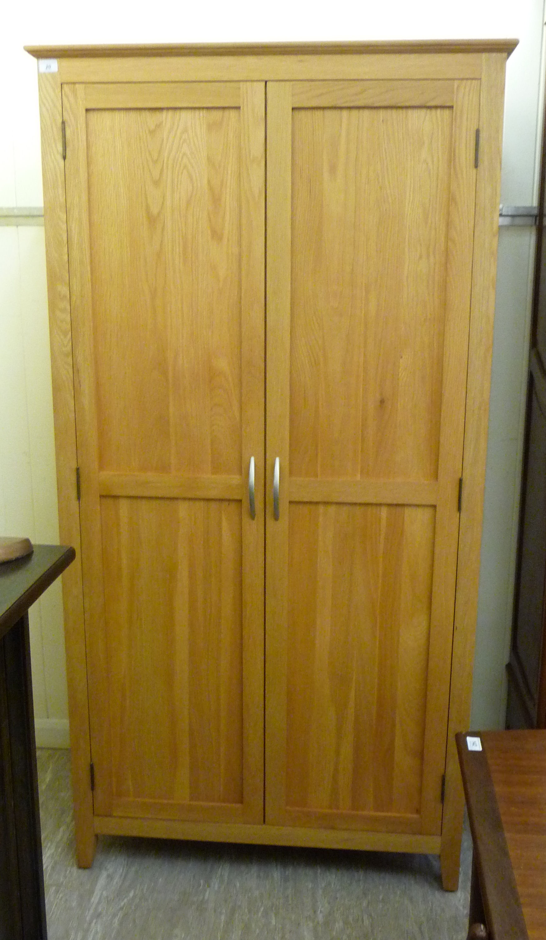 A modern light oak finished wardrobe with a moulded cornice, over a pair of panelled doors,