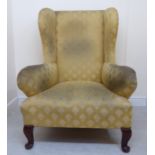 An early 20thC Georgian style wingback armchair, upholstered in patterned yellow fabric,