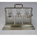 An early 20thC silver plated tantalus with bead bordered ornament and a lockable,