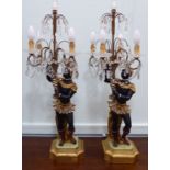 A pair of 20thC candelabra, each fashioned as a standing blackamoor, holding aloft a gilded,