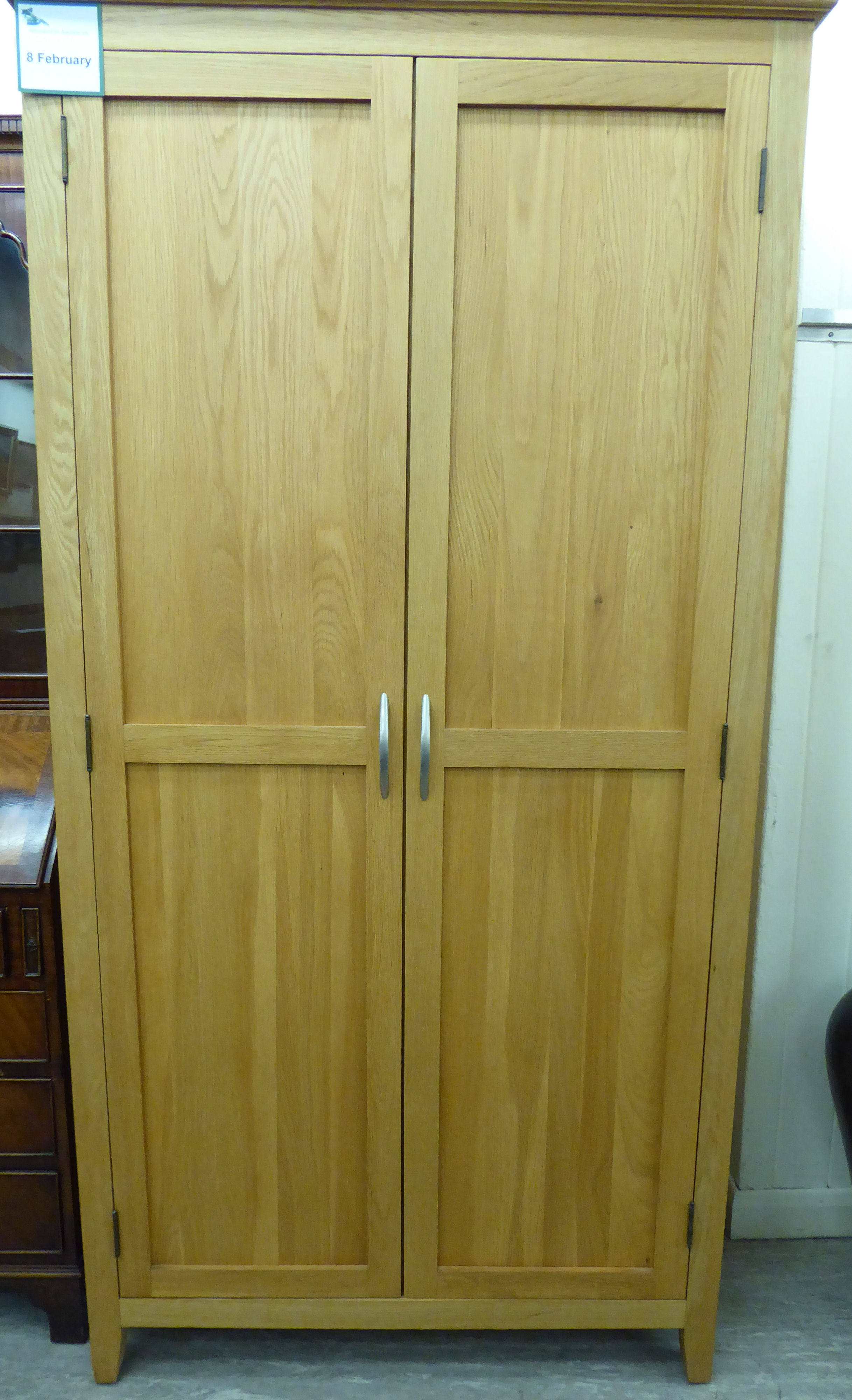 A modern light oak finished wardrobe with a moulded cornice, over a pair of panelled doors,