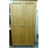 A modern light oak finished wardrobe with a moulded cornice, over a pair of panelled doors,