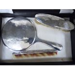 A three piece silver backed dressing table set comprising a hand mirror,