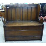 A mid 20thC Georgian style oak settle with a carved, planked wing back,