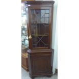 A modern mahogany finished standing corner cupboard with a glazed door, over a cupboard door,