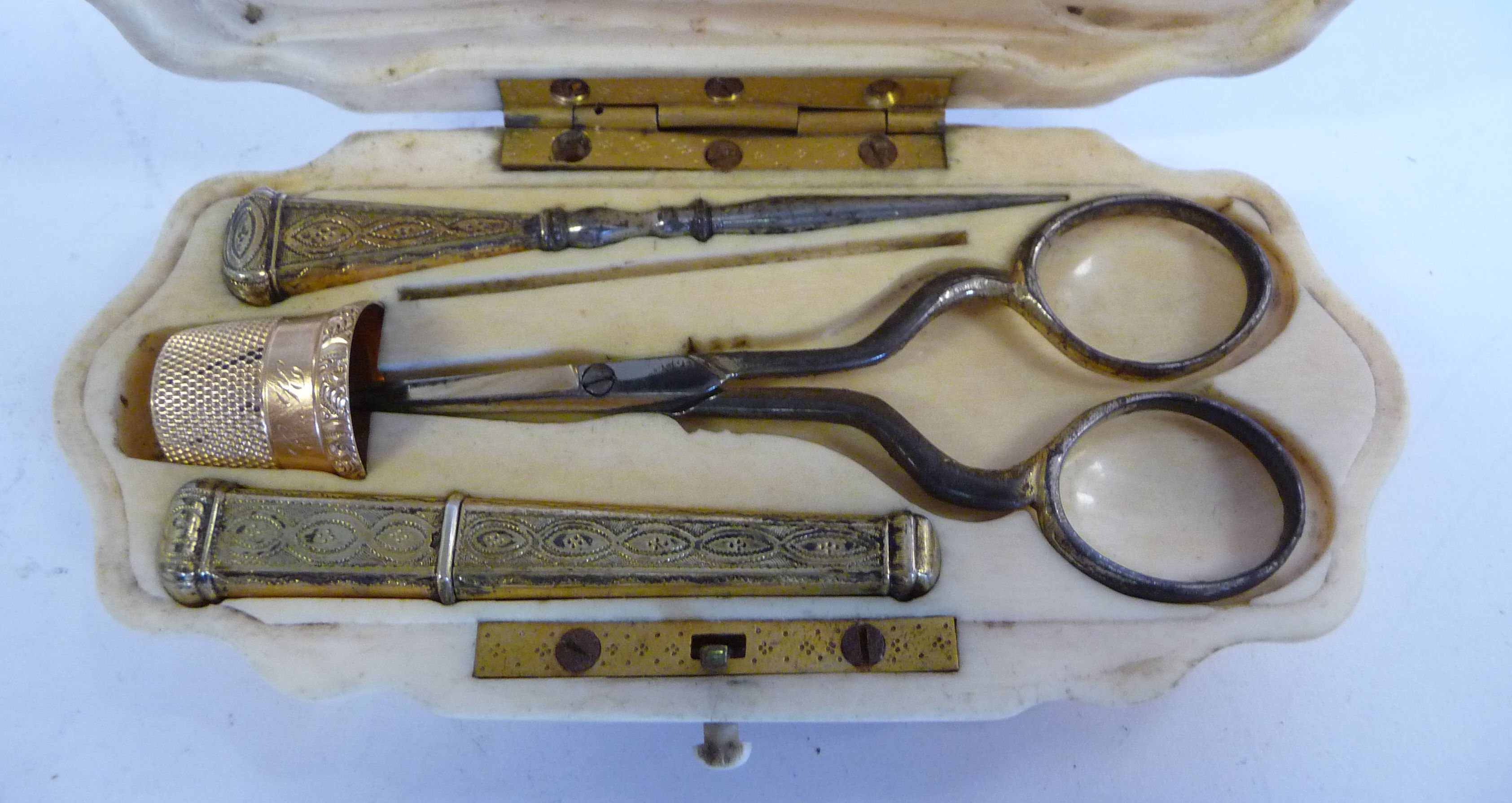 A mid Victorian carved ivory folding needlework case with yellow metal mounts and various