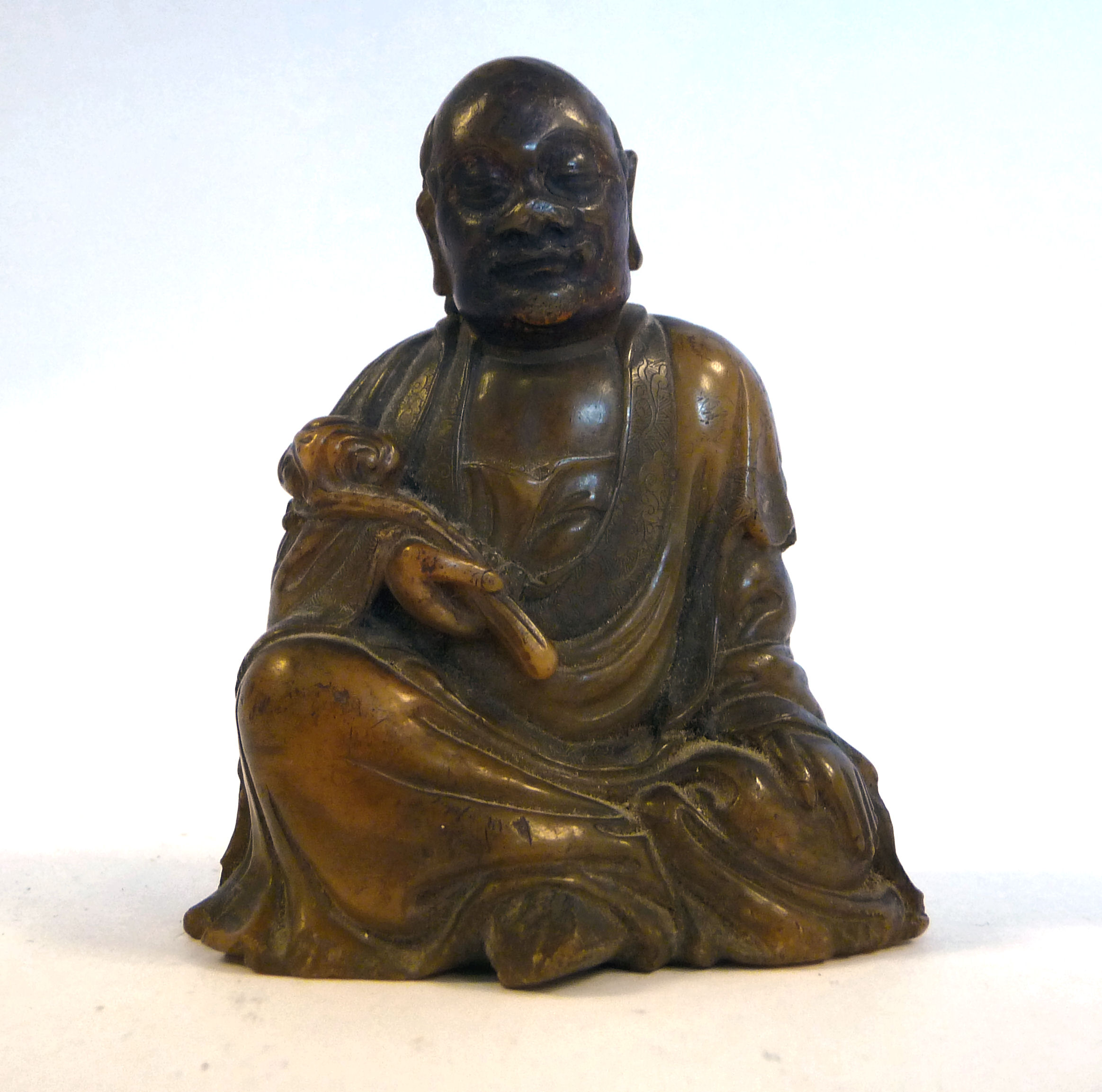 A 19thC Chinese carved brown soapstone seated, robed figure holding a lotus flower,